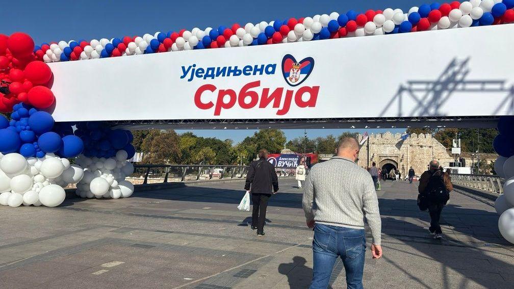 Velika improvizovana ograda na kojoj piše Ujedinjena Srbija, nekoliko ljudi prolazi ispod nje, a u daljini je na zidini Niške tvrđave postavljen veliki poster sa likom Aleksandra Vučića 